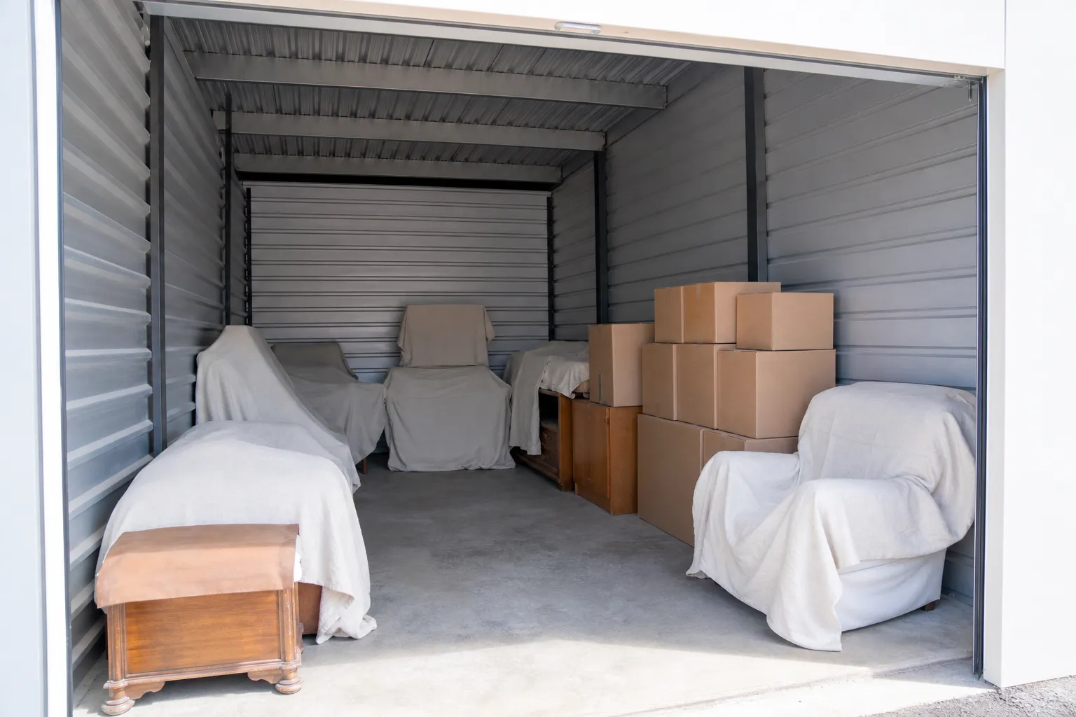 Intérieur d’un box de stockage avec meubles en bois housés et cartons rangés, espace de circulation laissé libre