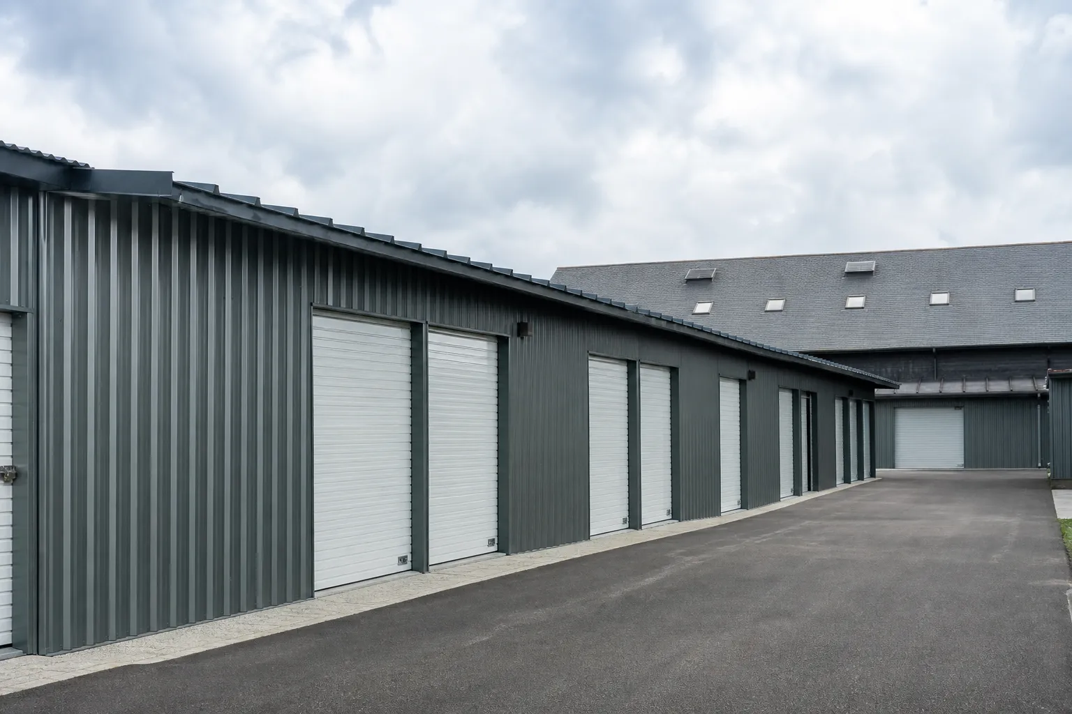 Devanture d’un centre de stockage au bardage zinc gris-vert, toiture d’ardoise en arrière-plan, allée d’accès dégagée